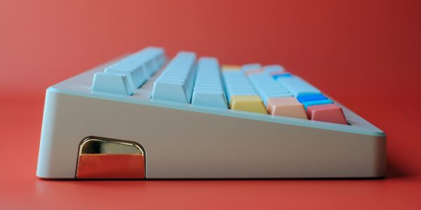 A close-up side view of a retro-styled mechanical keyboard with pastel-colored keys on a red background, conveying a playful and modern tone.