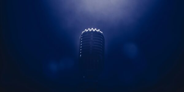 A vintage microphone stands alone in a dark, misty blue spotlight, evoking a sense of anticipation and nostalgia in a serene, focused atmosphere.