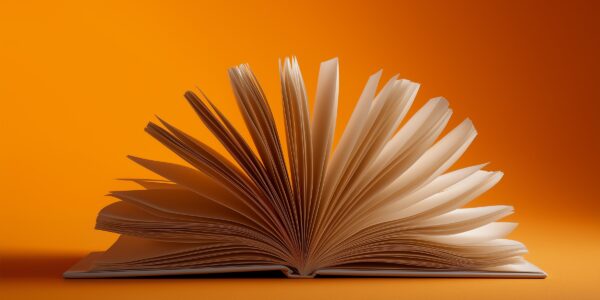 An open book with pages fanned out on an orange background, creating a sense of motion and creativity. The image conveys a warm and inviting tone.