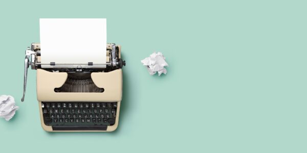 A vintage typewriter with a blank sheet of paper is centered on a pastel green background, surrounded by crumpled paper balls, suggesting a creative process.
